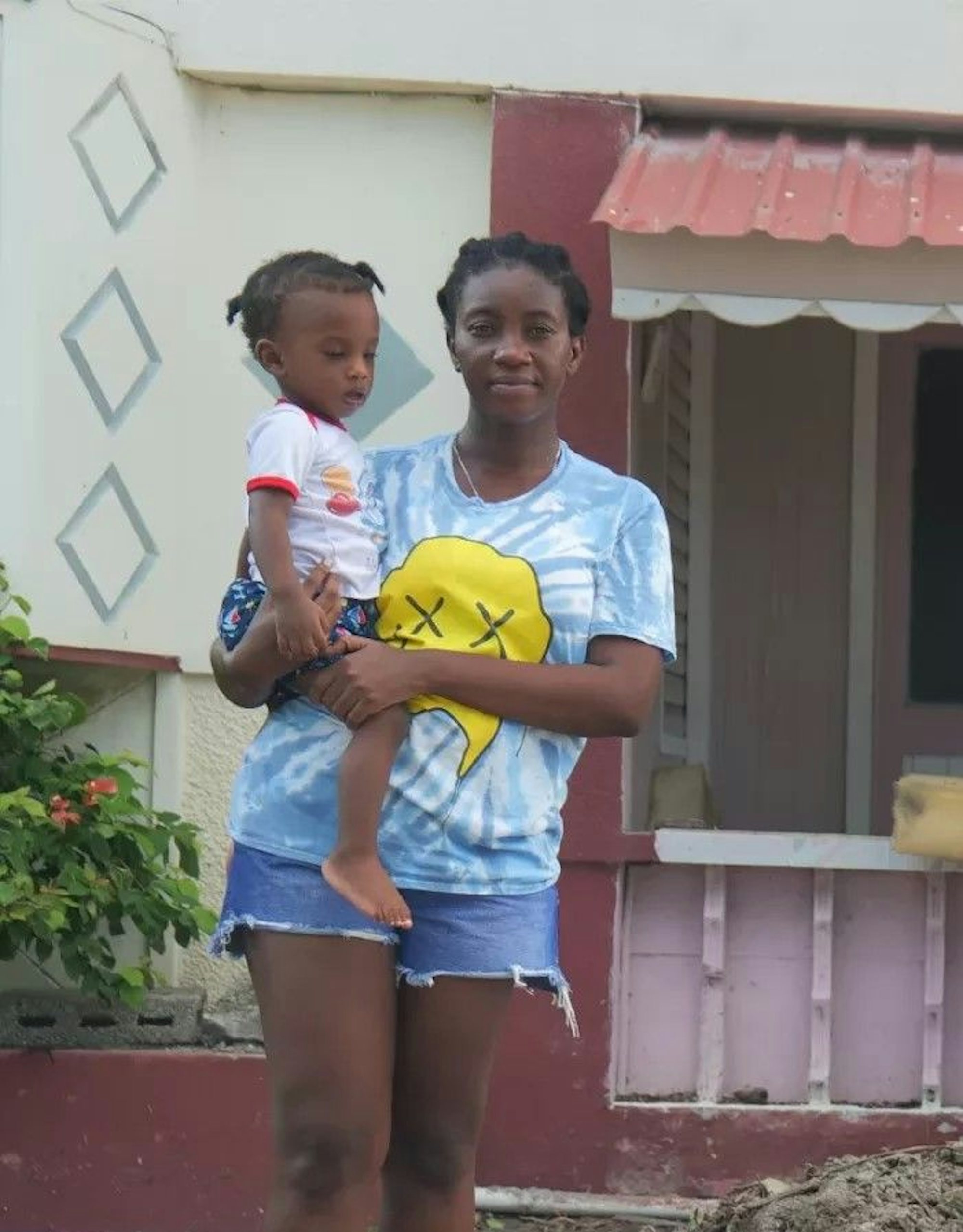 A woman holding a girl stands in front of a house