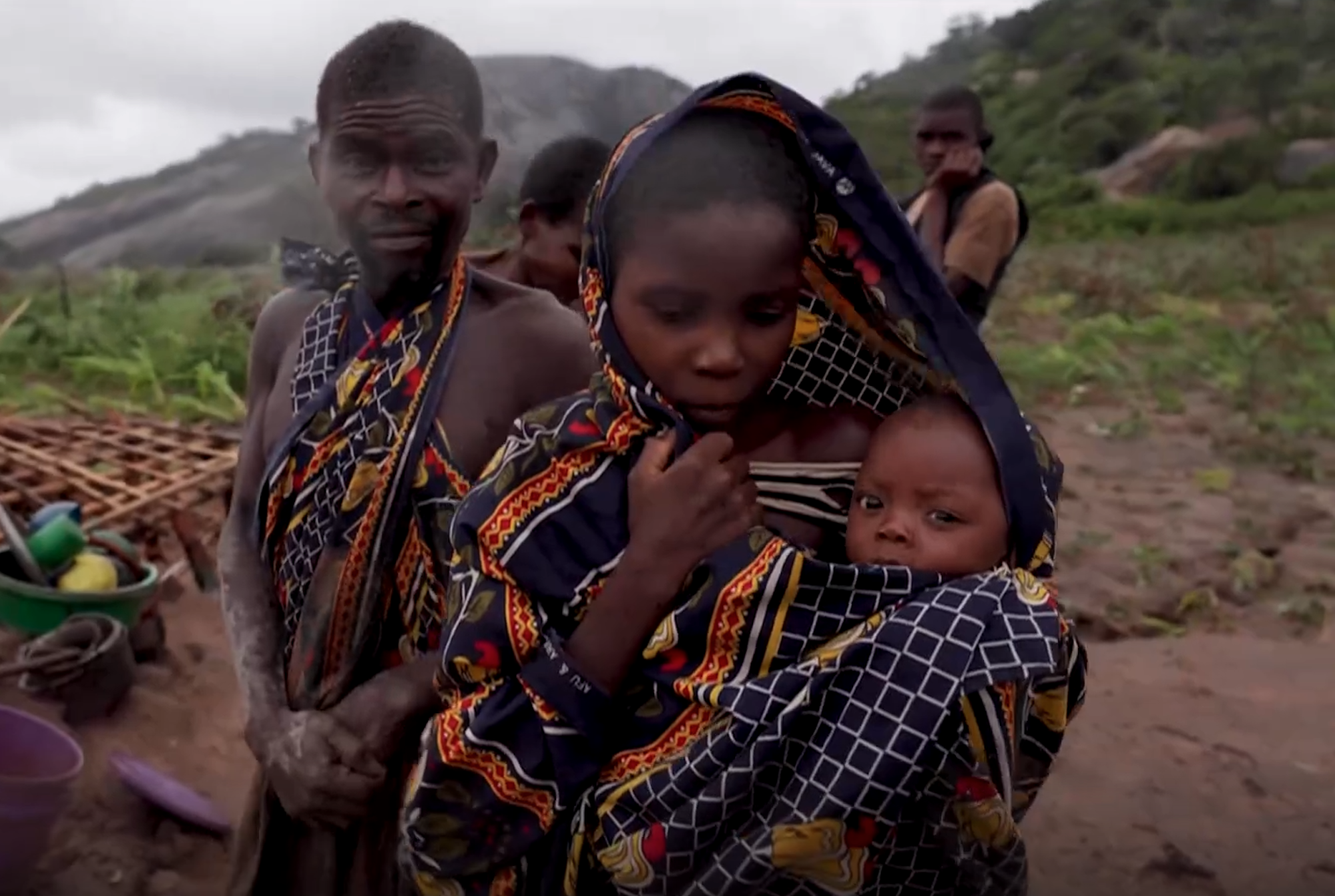 A man, woman and her child in a field surrounded by cyclone destruction.